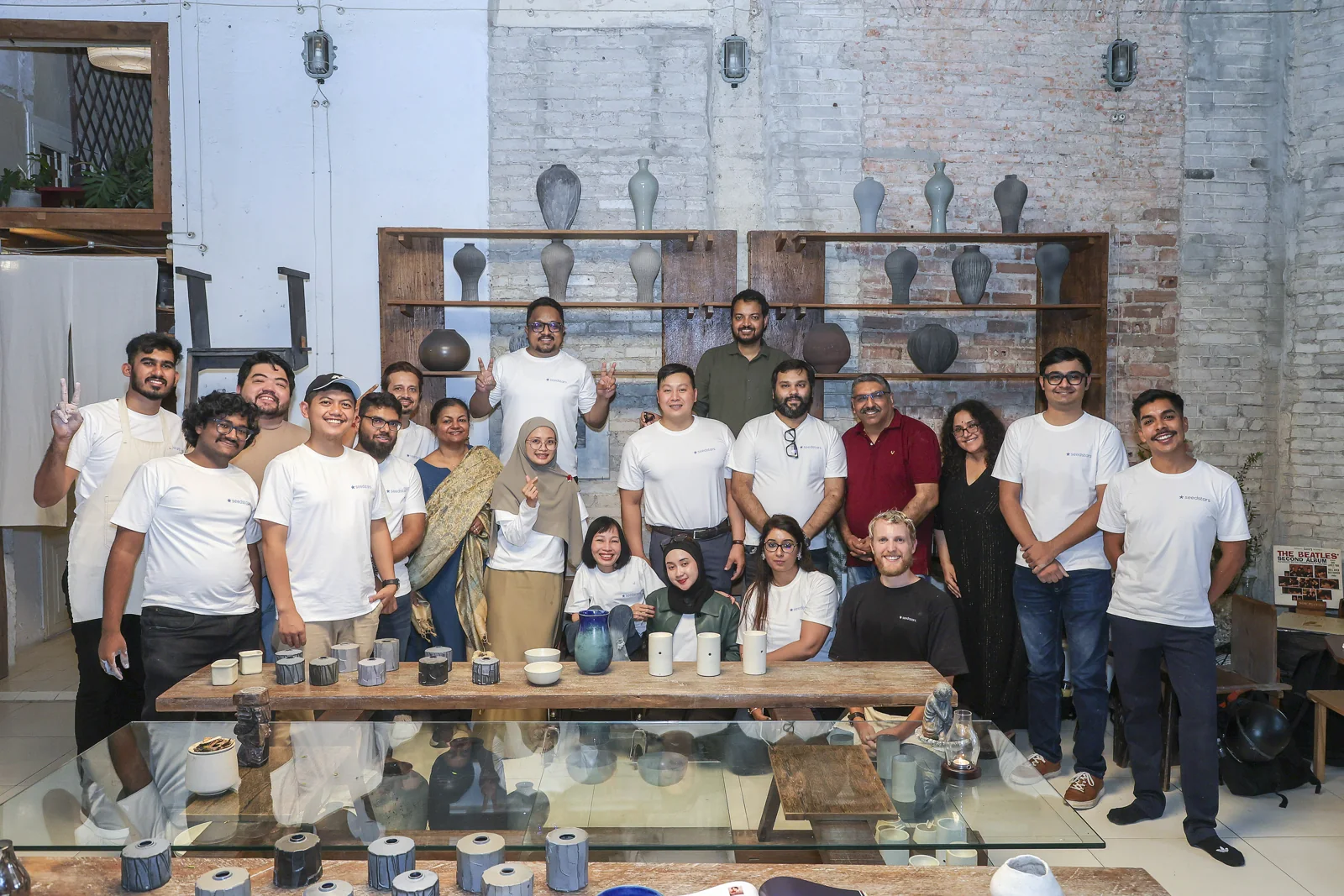 A group poses behind a table displaying handmade ceramics at a pottery studio.